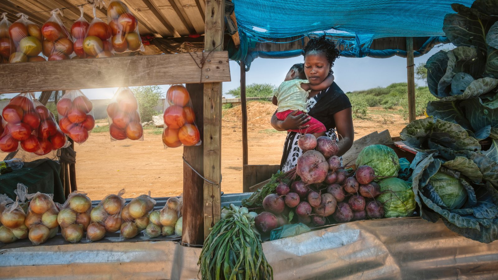 A woman holding her child at her market stall of fresh produce